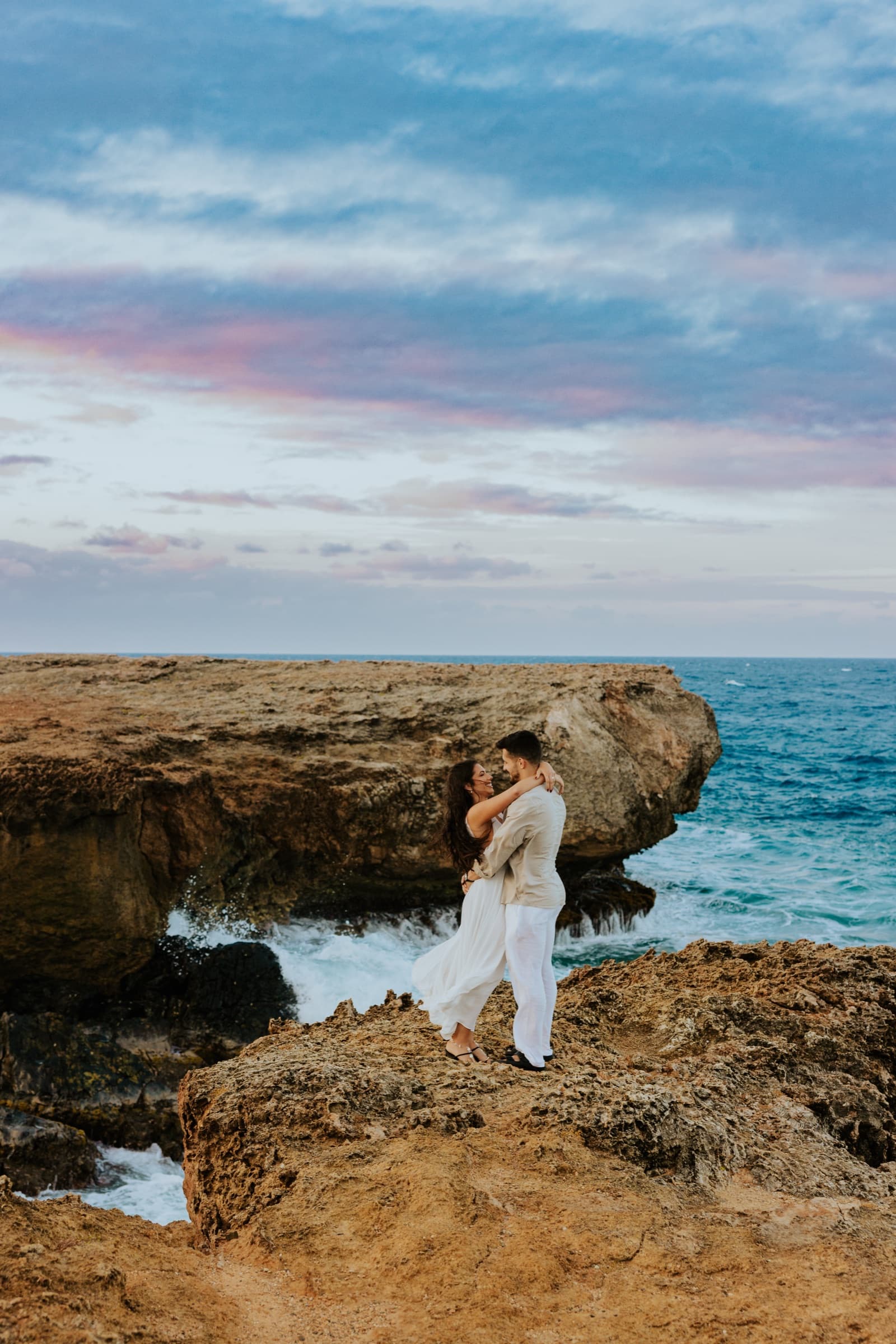 Julia and Ben embracing on the cliffs above the sea